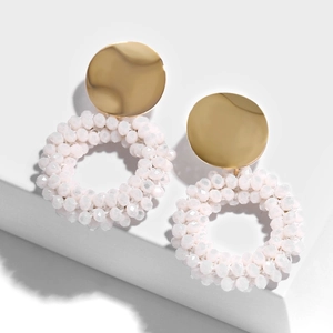 Detail of white beaded hoop earrings with gold metal disc on minimalist background