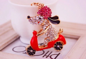 Close-up of sparkling rhinestone puppy riding a red scooter keychain with gold hardware