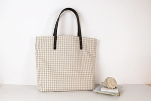 Close-up of the beige plaid canvas tote bag featuring premium brown leather handles