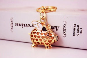 Macro view of a gold-toned winged pig keychain with heart-shaped cutout and enamel wings