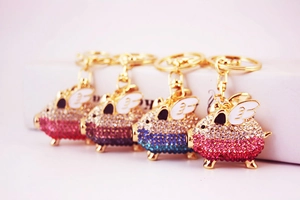Close-up of four colorful rhinestone-encrusted flying pig keychains in gold metal finish