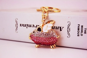 Detail of creative flying pig keychain with pink gradient rhinestones on a white book