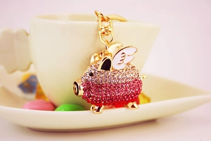 Pink rhinestone flying pig keychain with gold wings placed in a white ceramic cup
