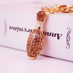Golden bowling pin keychain with brown crystals shown against a vintage book background