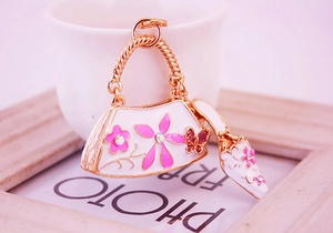 Macro shot of gold enamel keychain with rhinestone flowers, white bag and high heel