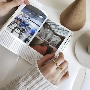 Detailed view of a gold chain ring featuring a geometric clasp on a hand with magazines