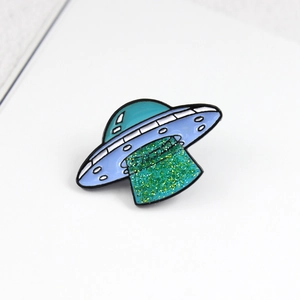 Macro shot of UFO enamel pin with purple finish and sparkling green glitter light beam