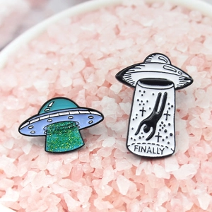 Close-up of a creative UFO enamel pin set with FINALLY text and green glitter details