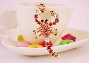 Close-up of golden scorpion keychain with brown rhinestones hanging on a white cup