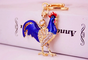 Detail of a golden rooster keychain with blue enamel inlay and sparkling crystal accents
