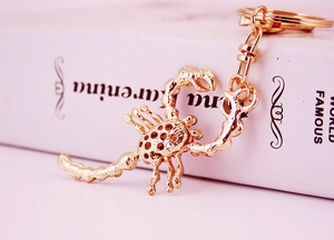 Detailed view of a golden metal scorpion keychain with crystal rhinestones on a book
