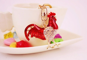 Close-up of red enamel rooster keychain with rhinestones hanging on a white ceramic cup