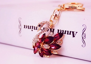 Detailed macro shot of a golden crystal swan keychain with red rhinestones on a white book