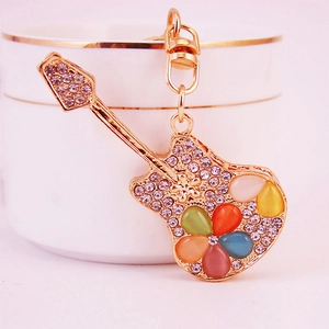 Golden guitar keychain with sparkling rhinestones and colorful cat eye stones beside a white cup