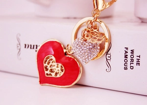 Close-up of gold keychain with red hollow heart pendant and small rhinestone heart charm