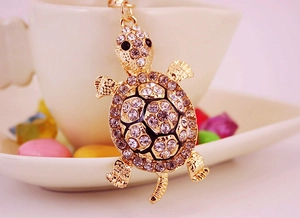 Close-up of golden turtle keychain with sparkling crystals on a ceramic cup saucer