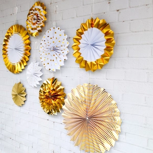 Set of 8 gold and white party paper fans with foil patterns on a white brick wall