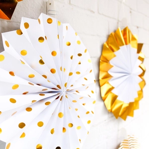 Set of 8 gold foil paper fans with polka dots and pleated edges on white brick wall