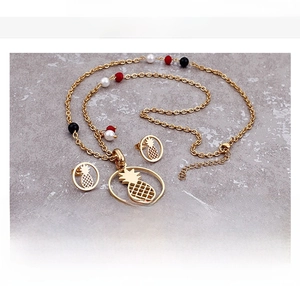 Flat lay of gold pineapple necklace and earrings set with colored beads on stone background