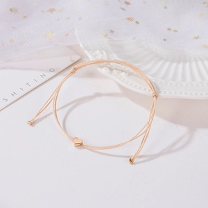 Détail d'un bracelet en cordon tressé beige avec charm cœur doré et nœud coulissant réglable