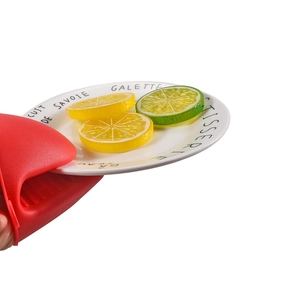 Red shark silicone heat resistant oven mitt lifting a white ceramic plate with lemon slices