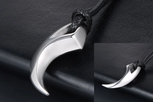 Detailed view of a silver wolf claw pendant with a black braided cord on leather surface