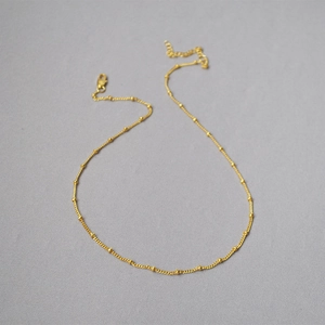 Dettaglio della collana minimalista con perline placcata in oro su sfondo grigio