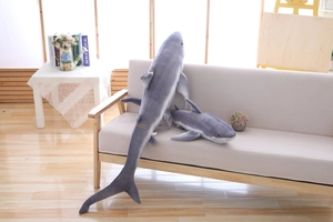 Close-up of two soft grey shark plush pillows in different sizes on a cozy sofa