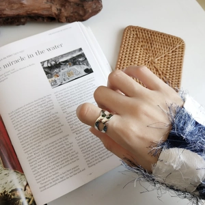 Detail shot of a silver knot-shaped chain ring worn on an index finger with props