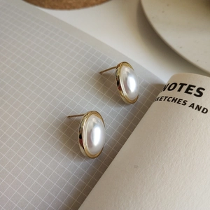 Macro shot of oval white shell pearl earrings with gold bezel on a textured background