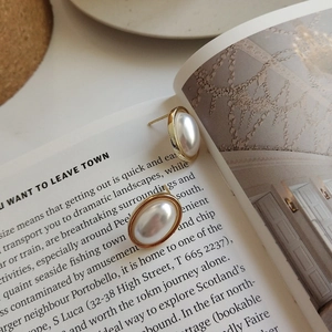 Elegant oval pearl stud earrings with gold plating on a vintage open book