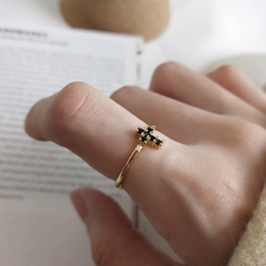 Minimalist gold cross ring with black zircon stones shown on a model hand