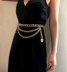 Detail of layered gold metal waist chain with coin pendant on a black dress
