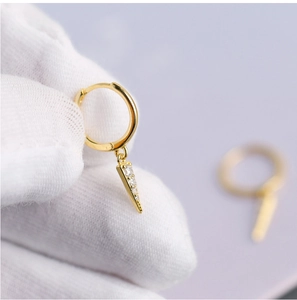 Close-up of gold triangular drop earrings with sparkling crystals held by a gloved hand