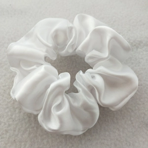 Close-up of a white satin scrunchie featuring smooth glossy texture and high elasticity