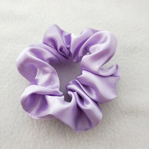 Detailed view of a purple satin scrunchie showing glossy fabric texture and soft pleats