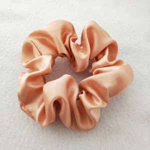 Detailed view of champagne satin scrunchie showing glossy silk texture and pleated fabric