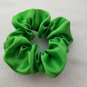 Detailed view of glossy green satin scrunchie with soft pleated texture on light surface