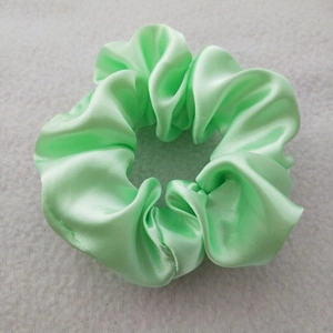 Detail of green satin silk scrunchie with high elasticity and elegant pleated fabric texture