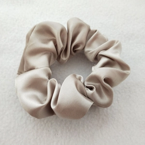Detail of a champagne satin scrunchie with a glossy silk texture and pleated design