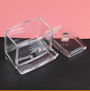 Close-up of clear acrylic cotton pad dispenser with lid on pink and black background