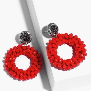 Detail of red beaded hoop earrings with crystal-studded studs on white geometric blocks