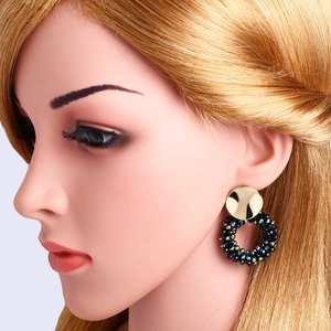 Close-up of golden disc studs with dangling woven dark crystal beads on model