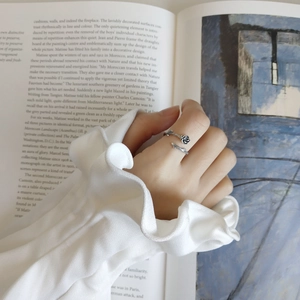 Artistic detail of a silver rose open ring worn by a model with a vintage book background