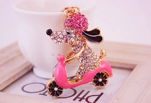 Detail of a gold puppy keychain with pink rhinestones on a scooter against soft pink decor