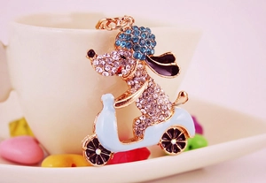 Detailed view of a rhinestone dog keychain riding a light blue motorcycle on white ceramic