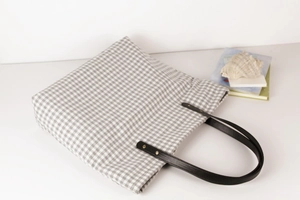 Flat lay of gray gingham tote bag with black leather handles and seashell decorations