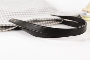 Close-up of leather handle with precise stitching on a grey gingham fabric shoulder bag