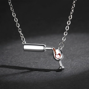Macro shot of silver wine bottle and glass pendant necklace with red heart zircon