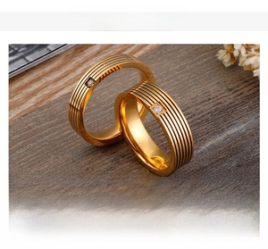 Close-up of golden titanium steel rings featuring horizontal grooved textures and inlaid stones
